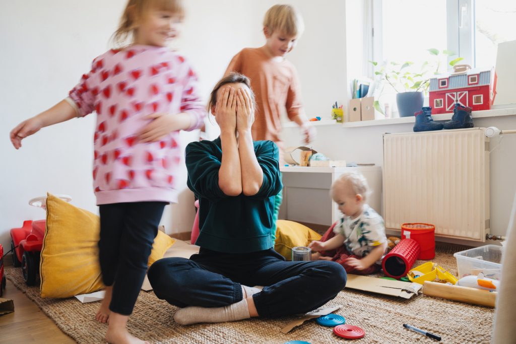 Majka sjedi na podu i pokriva lice dok djeca trče
