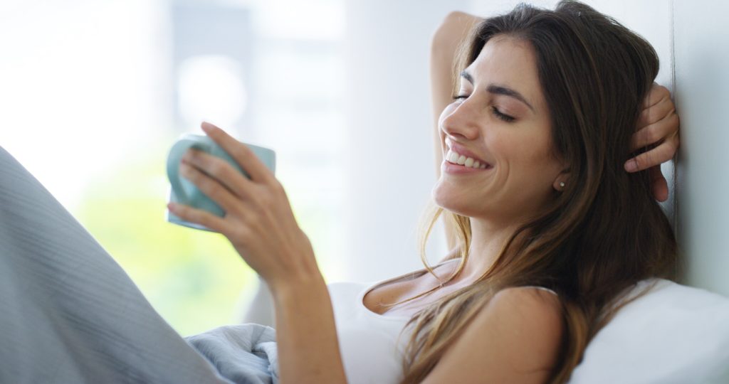 žena zadovoljna leži u sobi i pije čaj 